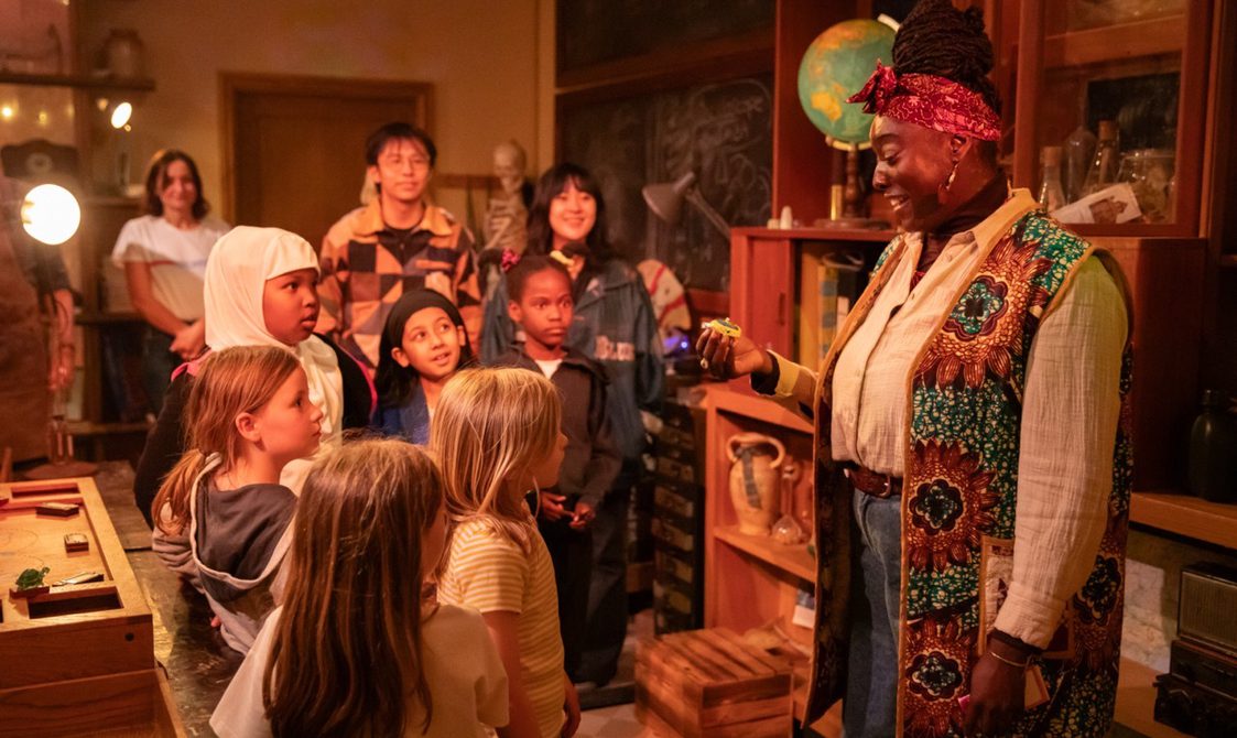 A group of children in an immersive theatre show looking and pointing at a performer.