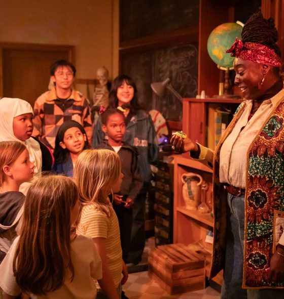 A group of children in an immersive theatre show looking and pointing at a performer.
