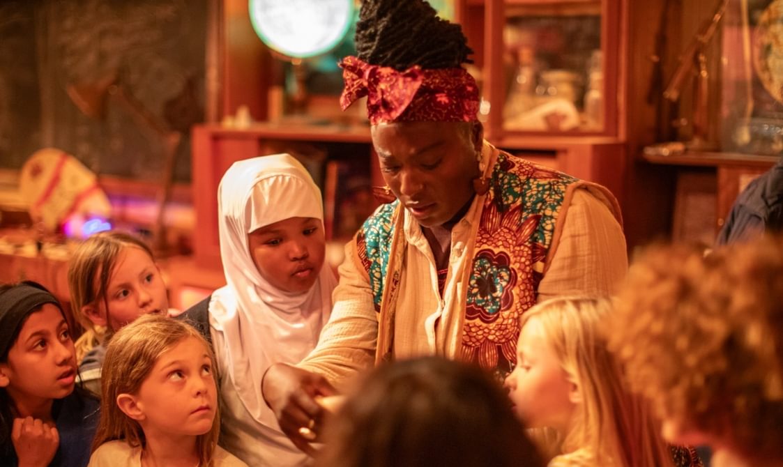 A group of children in an immersive theatre show looking at a letter held by a performer