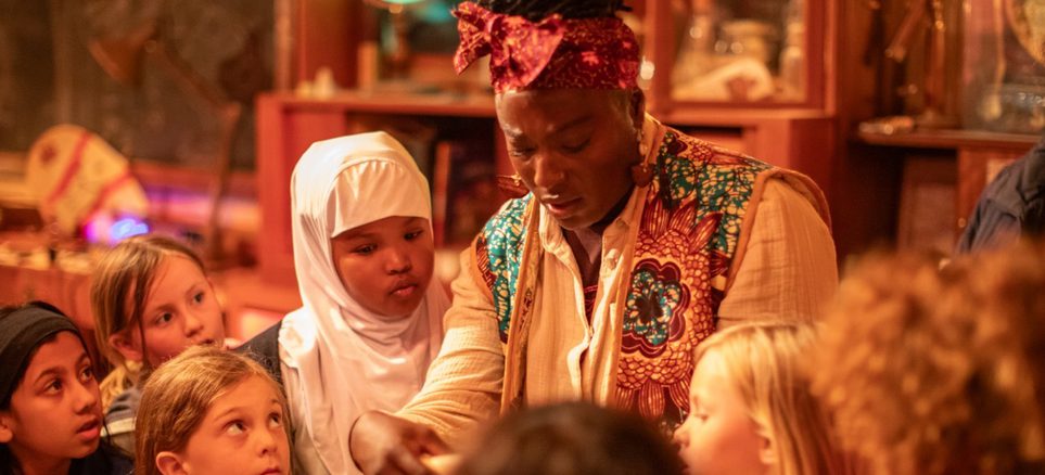 A group of children in an immersive theatre show looking at a letter held by a performer