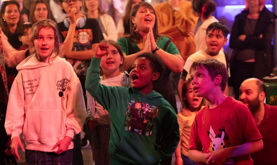 A group of children in an immersive theatre show cheering.