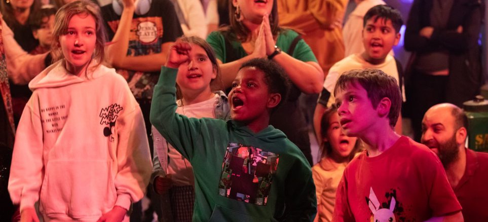 A group of children in an immersive theatre show cheering.