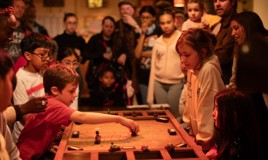 A group of children in an immersive theatre show playing a wooden board game.