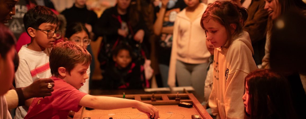 A group of children in an immersive theatre show playing a wooden board game.