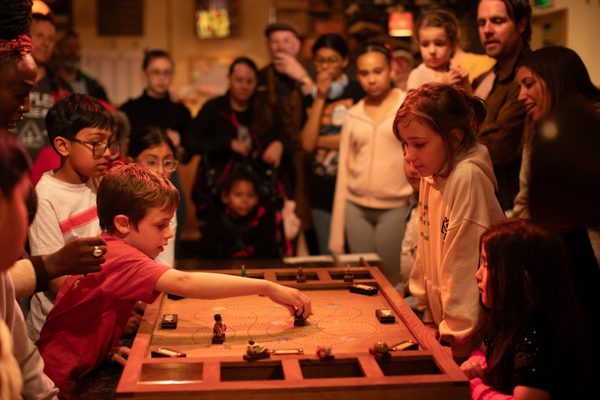 A group of children in an immersive theatre show playing a wooden board game.