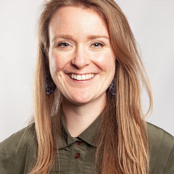 A headshot photograph of a white woman with long red hair wearing a green shirt smiling to camera.