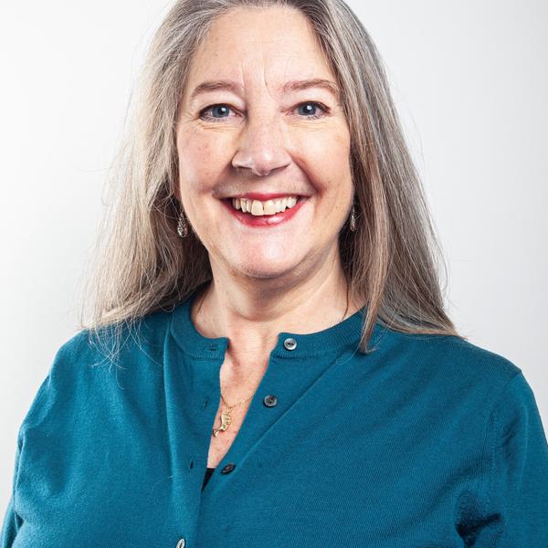 Headshot portrait photo of a white woman with long grey hair. She is wearing a teal coloured cardigan.