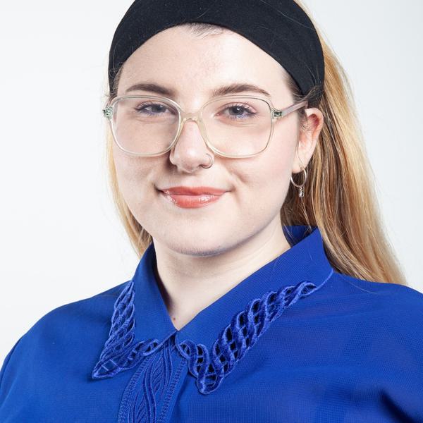 Headshot photograph of a white woman with long blonde hair. She is wearing a black headband, round glasses and a blue shirt.