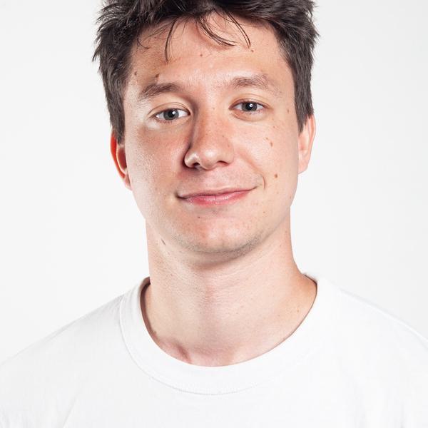 Headshot portrait photo of a white man with short brown hair wearing a white t shirt.