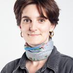 Headshot portrait photo of a white woman with short brown hair. She is wearing gold hoop earrings, a scrf and a green denim shirt.