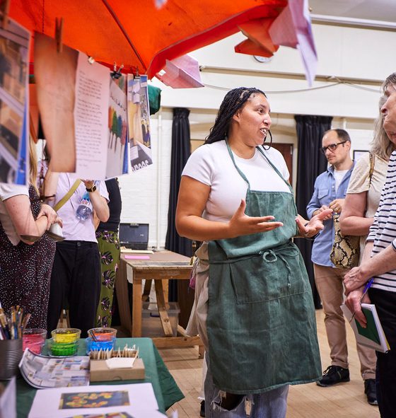 A group of people talking to each other at an indoor marketplace. There are images from immersive learning projects hung up with pegs on a laundry line.
