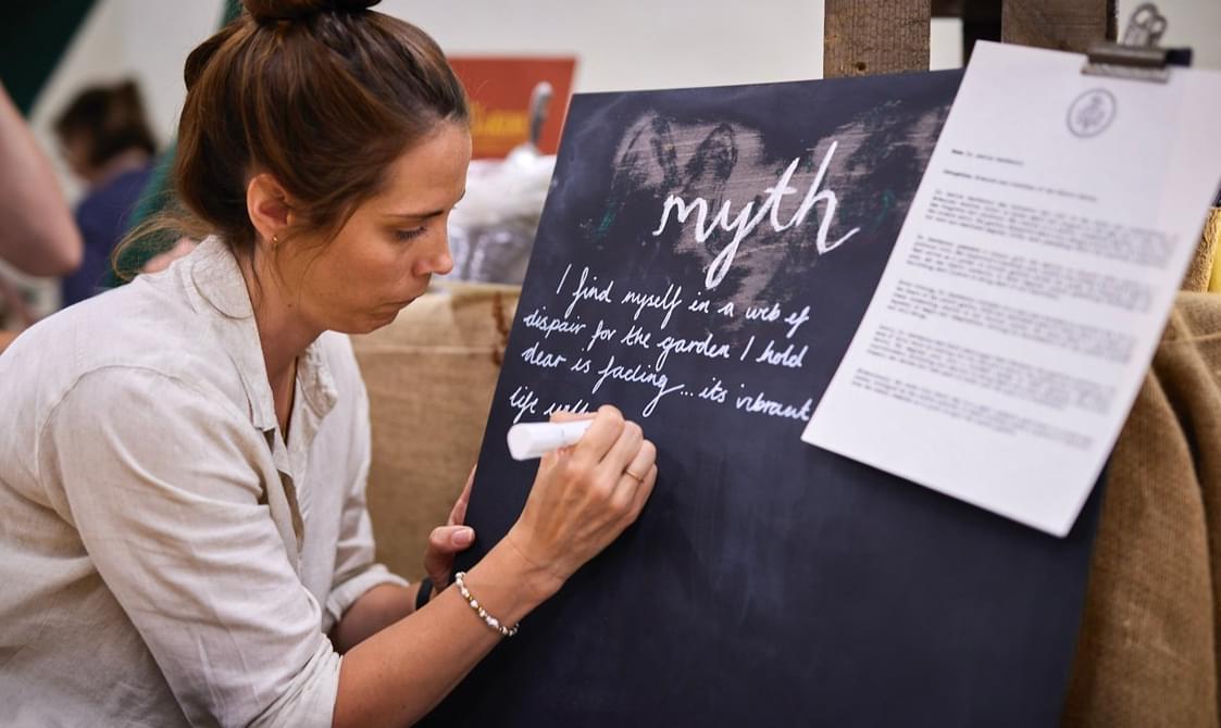 A woman wearing a white top writes about "myths" on a black chalkboard