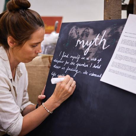 A woman wearing a white top writes about "myths" on a black chalkboard