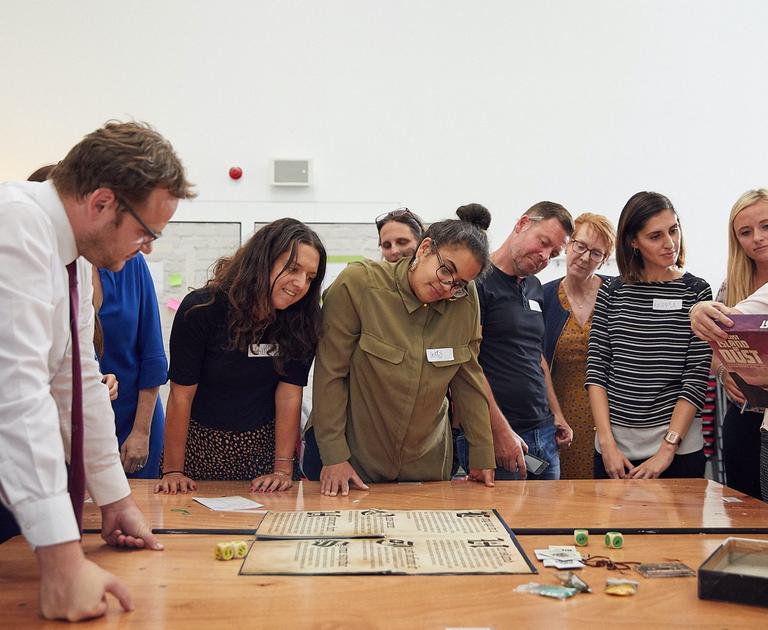 A group of people stand around a table and look at the map of a game.