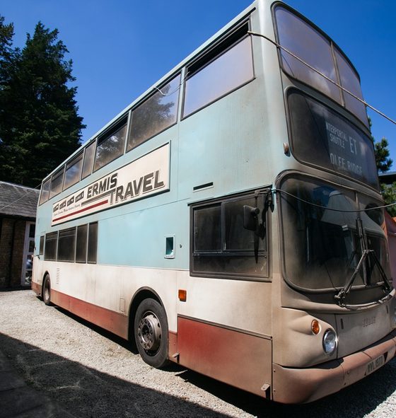 A dusty old double decker bus parked outside in the sunshine. It is a light blue at the top with white and red at the bottom.