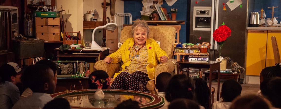 Elderly woman sat in an armchair in her living room in front of a group of children