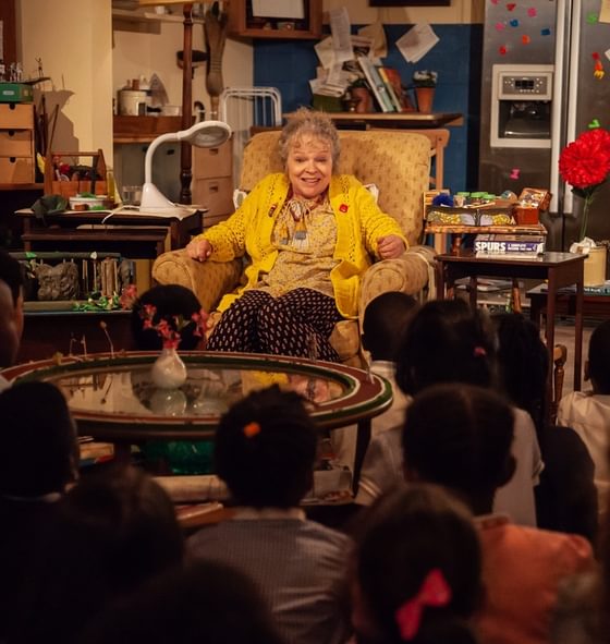 Elderly woman sat in an armchair in her living room in front of a group of children