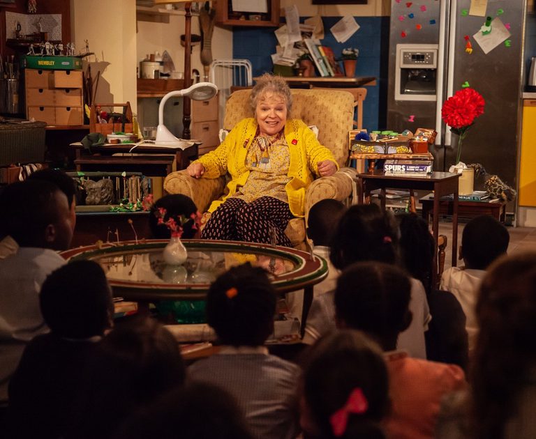 Elderly woman sat in an armchair in her living room in front of a group of children
