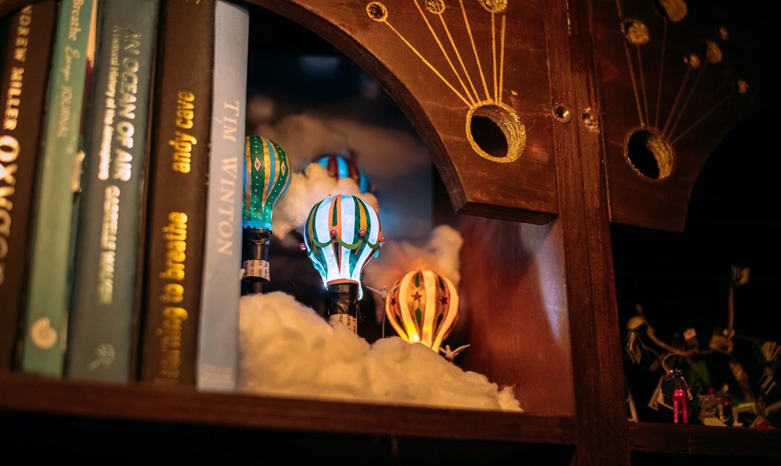 A close up image of a shelf with books and three light up miniature objects of hot air balloons.