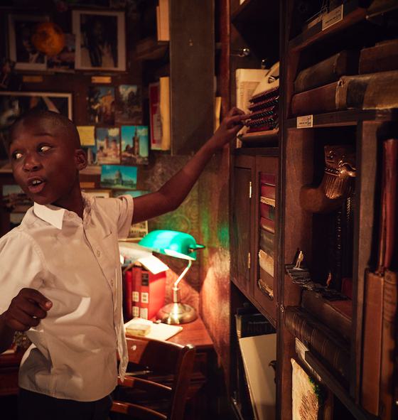 A young boy smiling and pointing at at a shelf of books in a dimly lit library