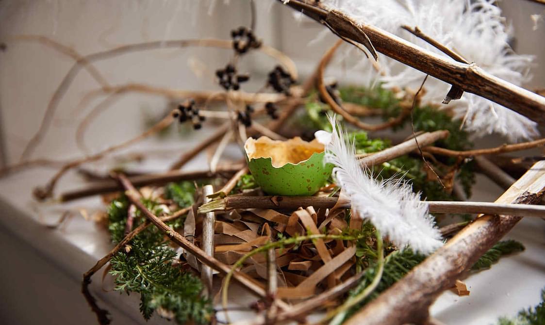 A nest on a window sill with a cracked gold and green egg.