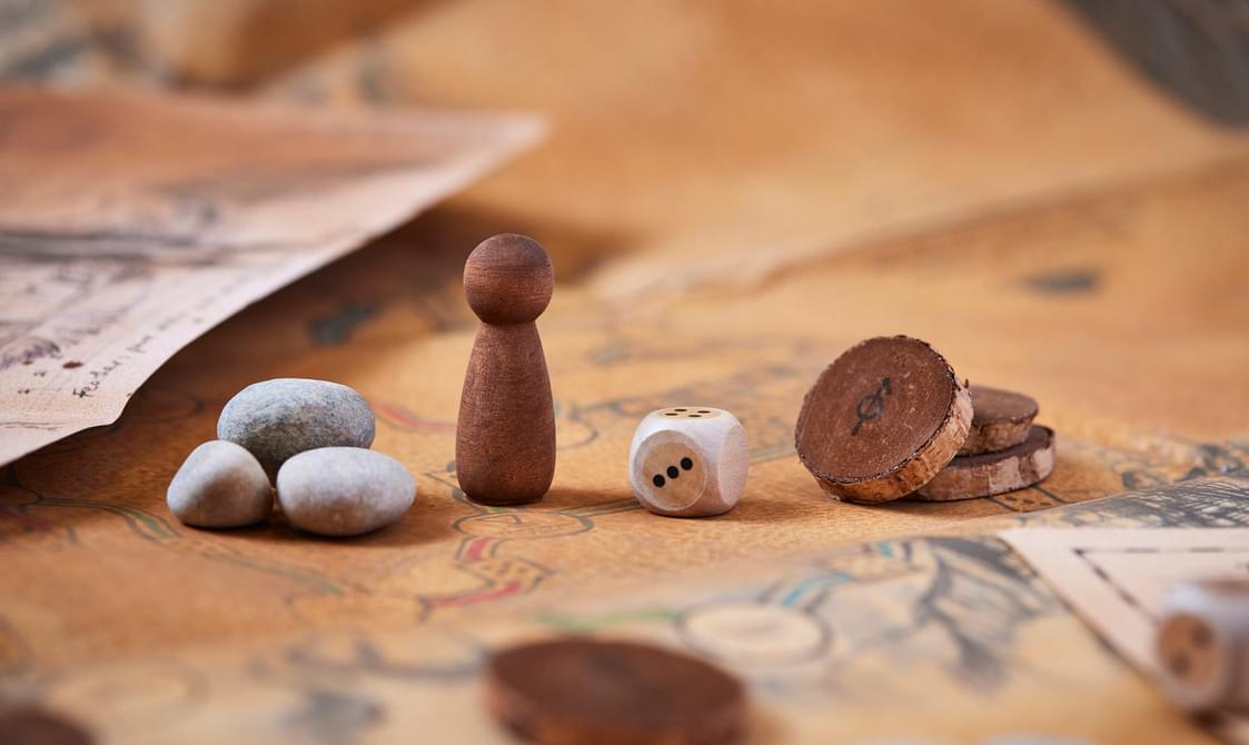 An old board game with wooden pieces, a dice and some grey stones.
