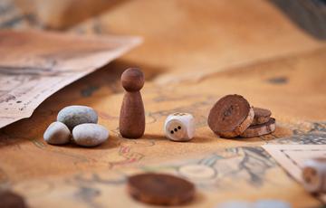 An old board game with wooden pieces, a dice and some grey stones.